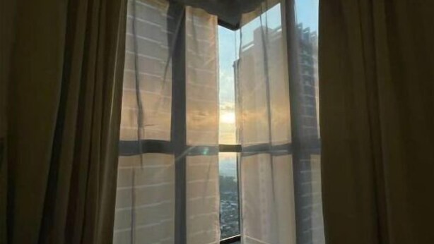 Une pièce avec une fenêtre d’angle, des rideaux et un lit.