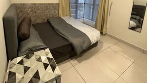 Une chambre avec un lit, une petite table, un ventilateur de plafond et une fenêtre avec des rideaux.