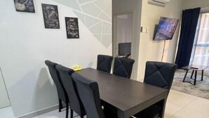 Un coin repas comprenant une table rectangulaire et six chaises, un téléviseur à écran plat fixé au mur, et un décor mural géométrique moderne.