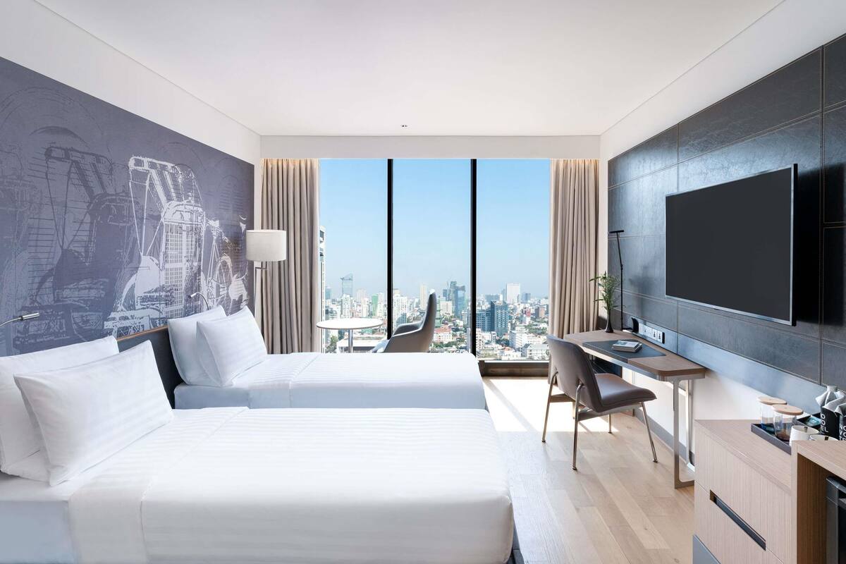 Une chambre d’hôtel moderne avec deux lits, un bureau, une télévision et une vue sur la ville.