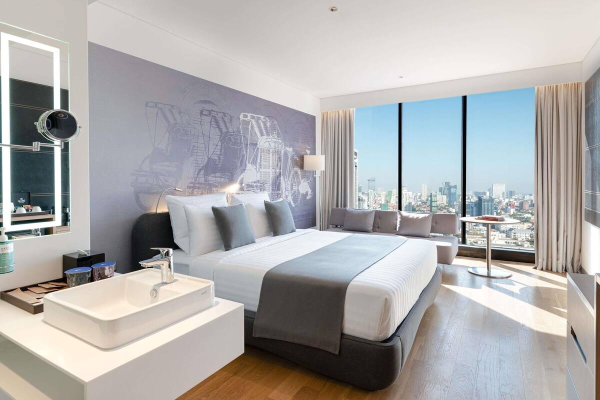 Une chambre d’hôtel moderne avec un grand lit, une salle de bain avec un lavabo blanc, une vue sur la ville et une grande fenêtre.