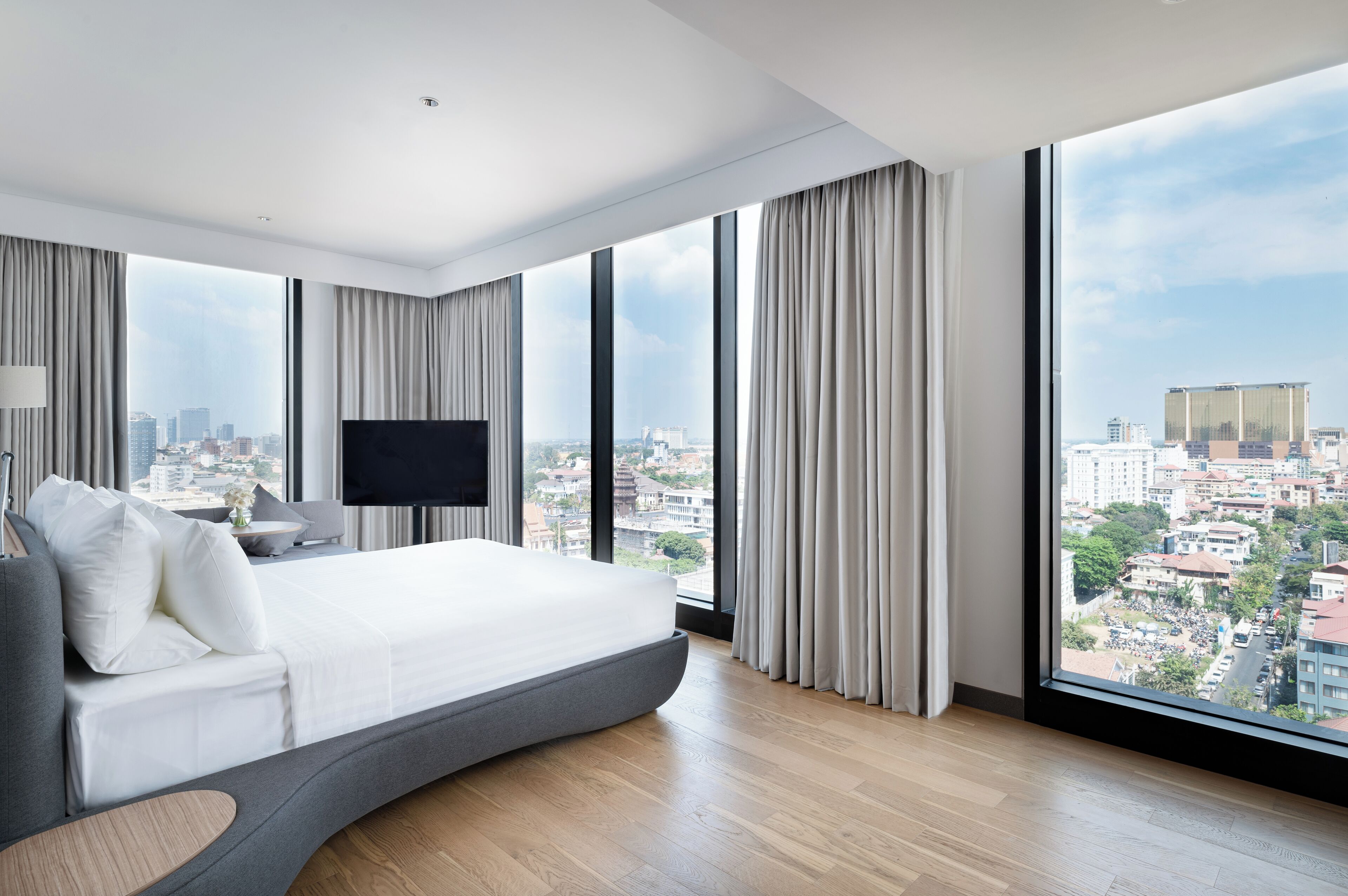 A modern hotel room with a curved bed, large windows, and a city view.