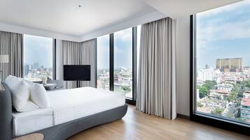A modern hotel room with a curved bed, large windows, and a city view.