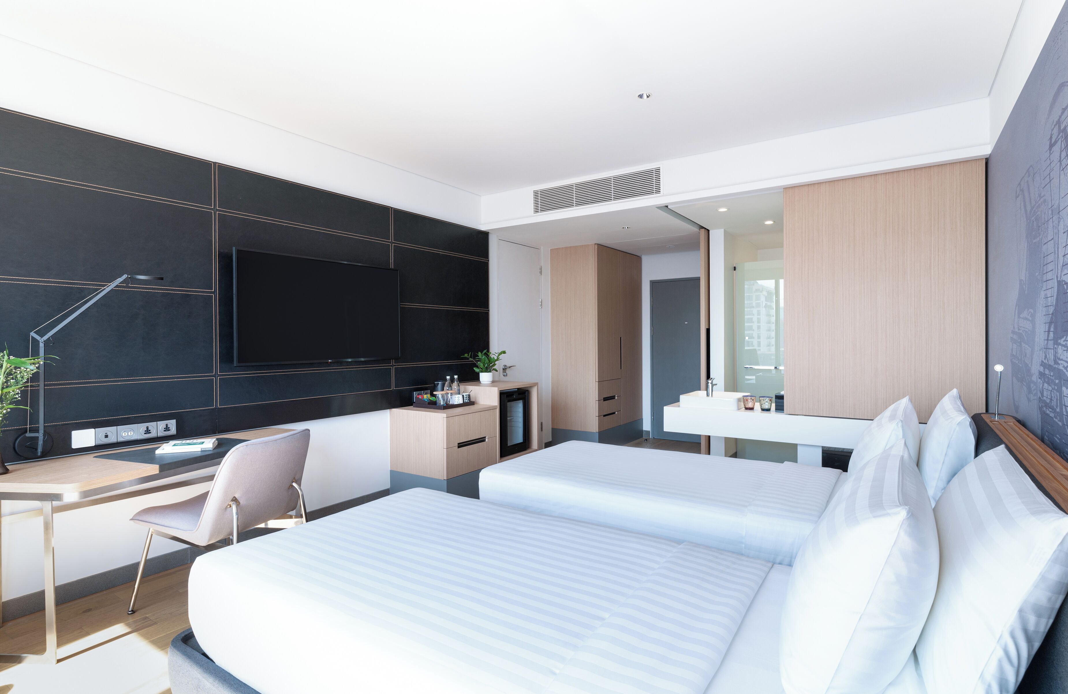Una habitación de hotel moderna con una cama grande, un escritorio, un televisor de pantalla plana, una kitchenette pequeña y un baño.