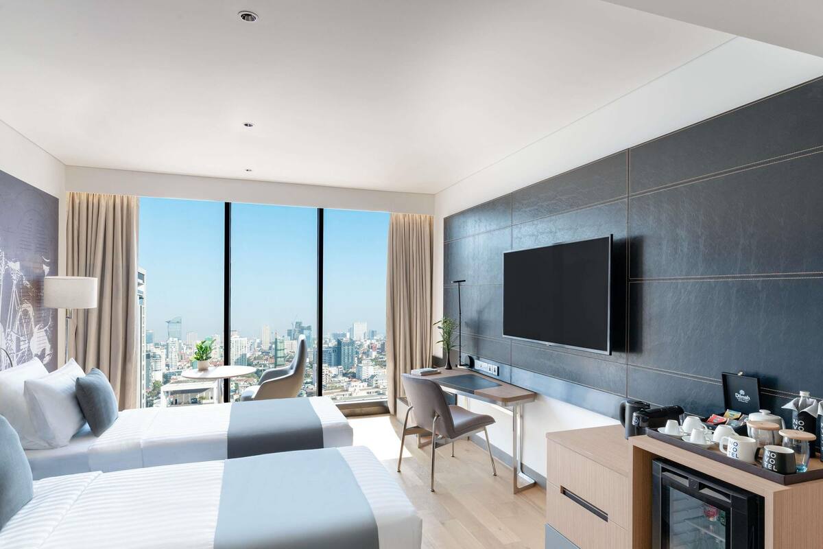 Une chambre d’hôtel moderne équipée de deux lits, d’un bureau, d’une télévision à écran plat et offrant une vue sur la ville.