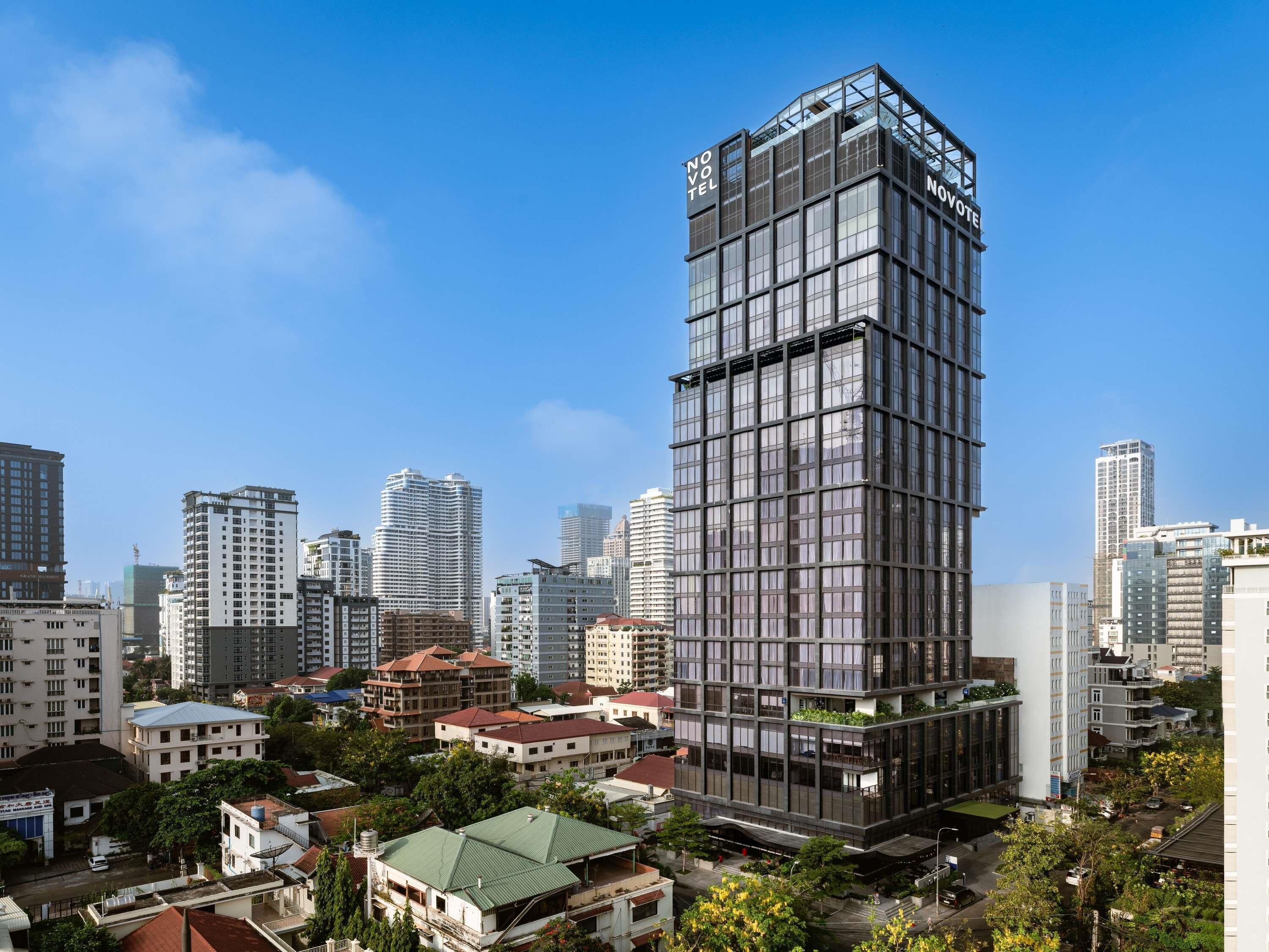 A modern high-rise hotel with a glass facade, surrounded by other buildings and greenery.