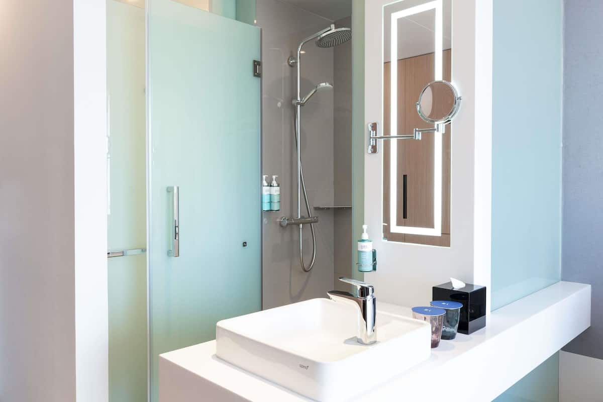 A modern bathroom with a white sink, a glass shower enclosure, and a mirror with a lighted frame.