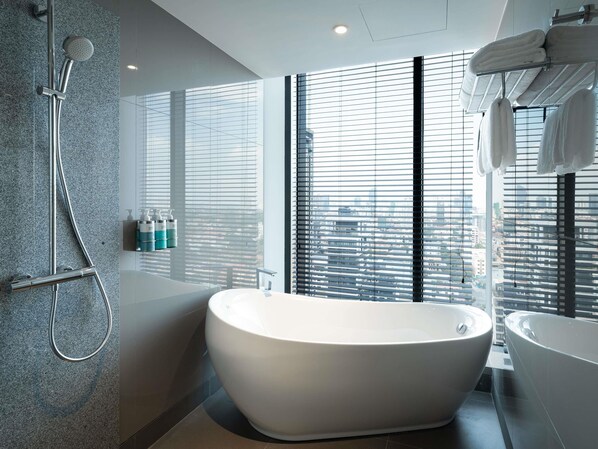 A modern bathroom with a freestanding bathtub, a showerhead, and a large window with blinds.
