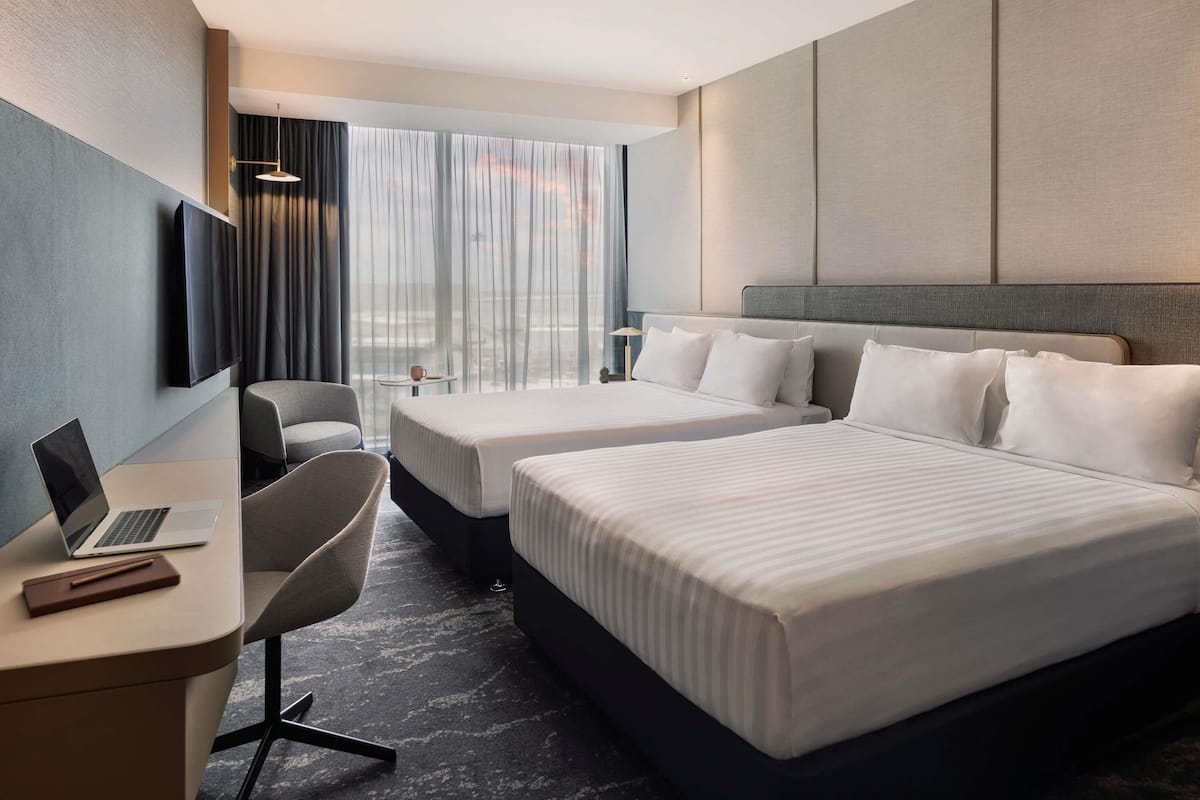 A hotel room with two beds, a desk with a laptop, a chair, and a TV mounted on the wall.