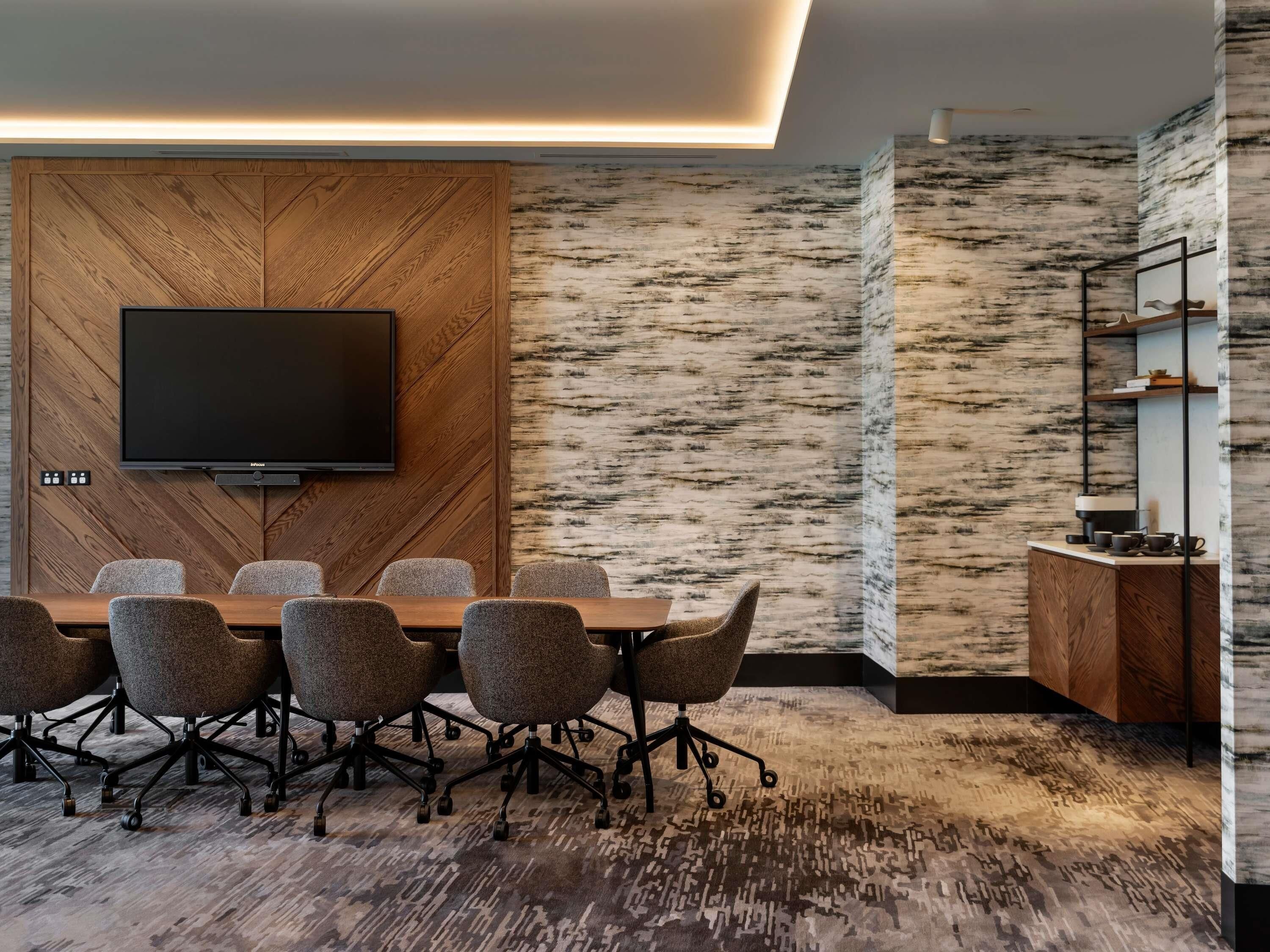 Ein Konferenzraum mit einer holzverkleideten Wand, einem Wand-Fernseher und einem gemusterten Teppich.