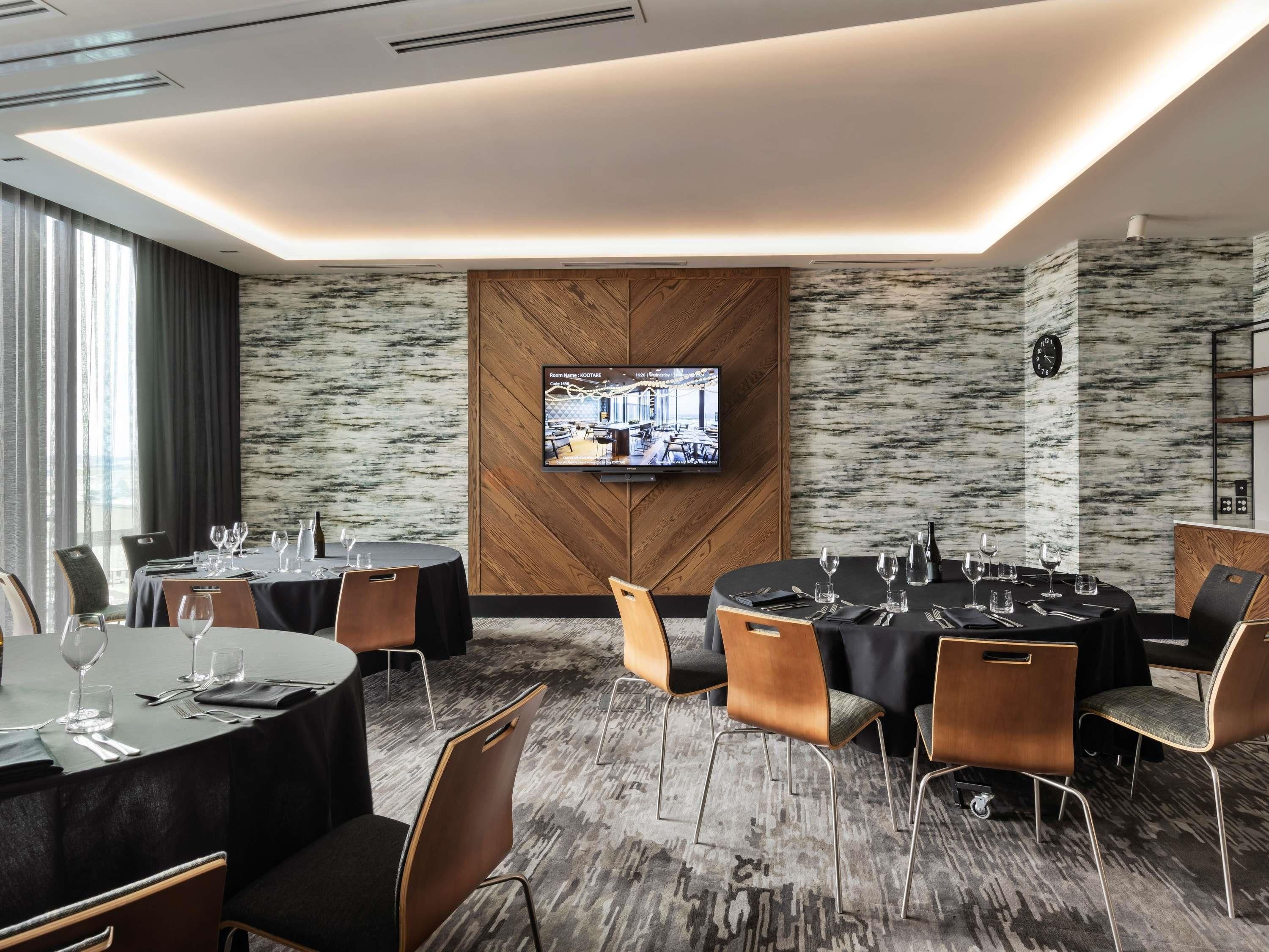 A modern hotel room with a large TV, multiple dining tables, and a patterned wall.