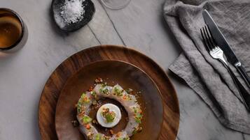 Un plato de madera con ceviche, una copa de vino blanco y un salero sobre una mesa de mármol.