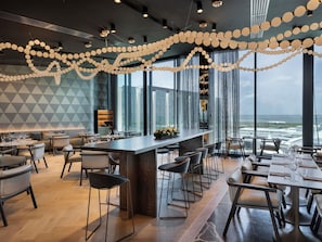 A modern restaurant with a bar area, large windows, and a view of the sea. - Pullman Auckland Airport (Auckland)
