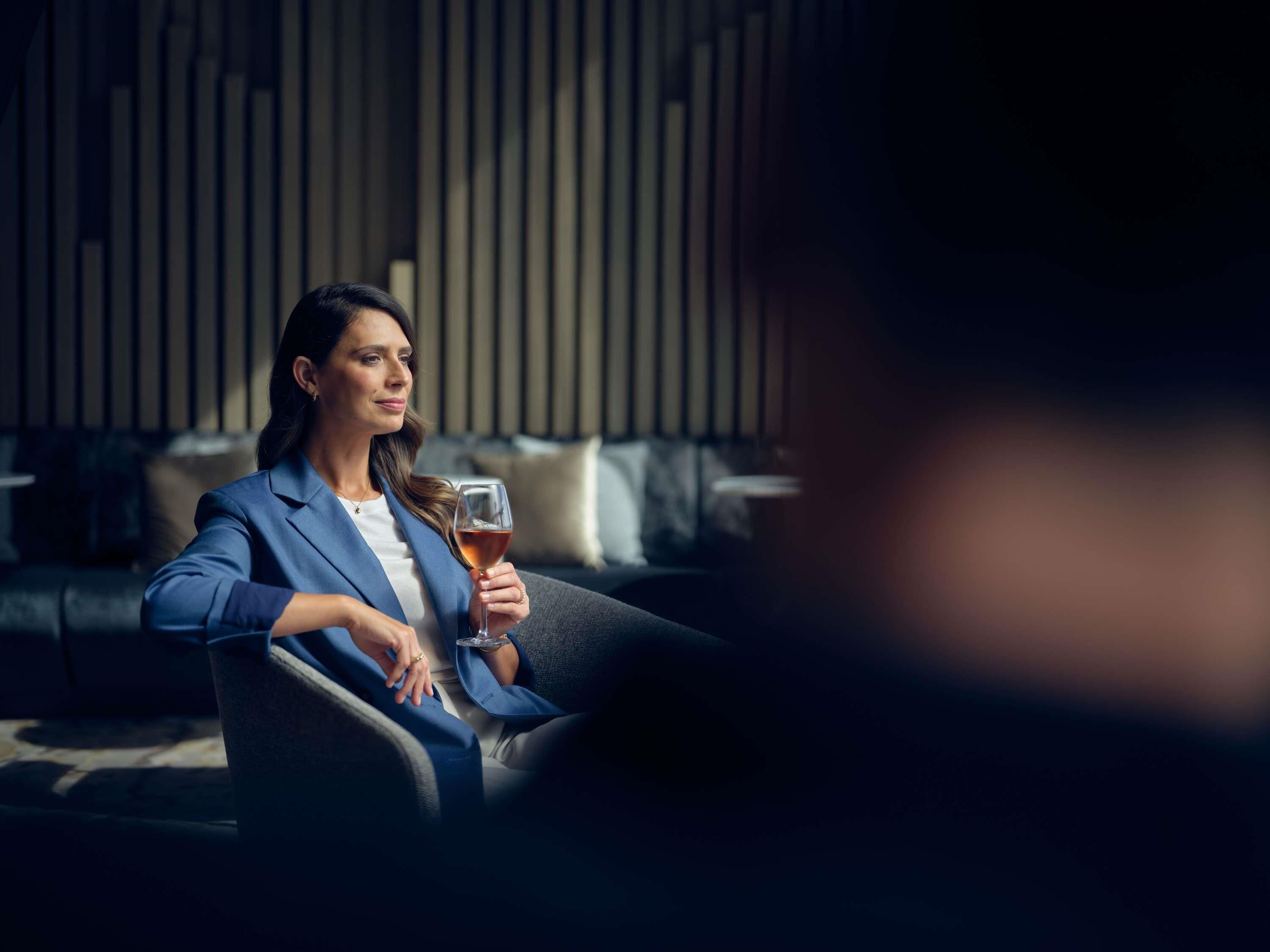 A person seated on a couch in a room with a modern design, holding a glass.