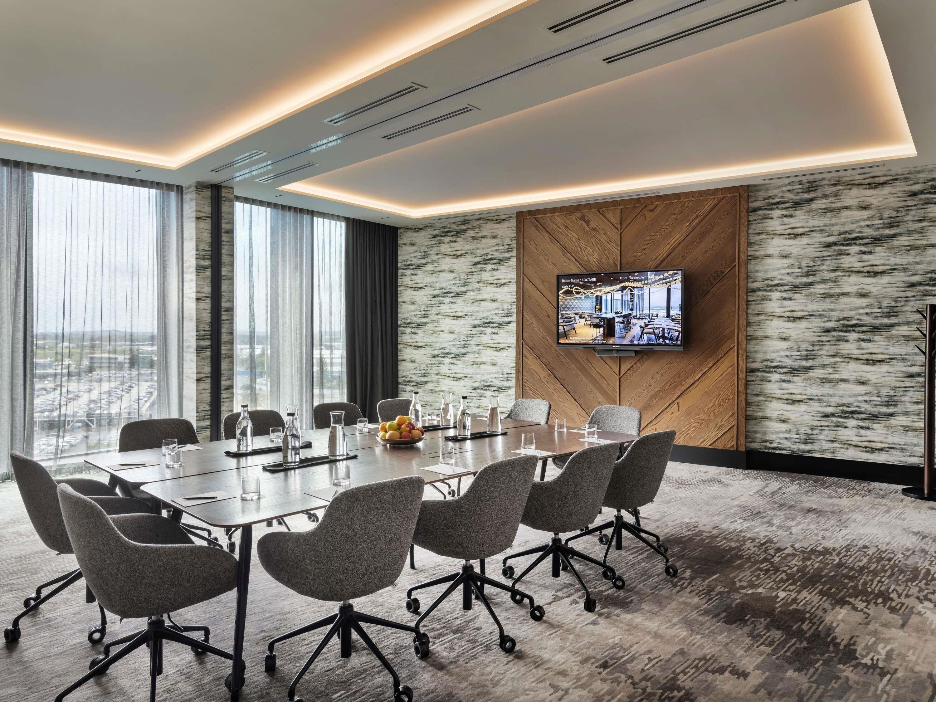Una sala de conferencias moderna con una gran mesa, sillas, una televisión y vistas a la ciudad.