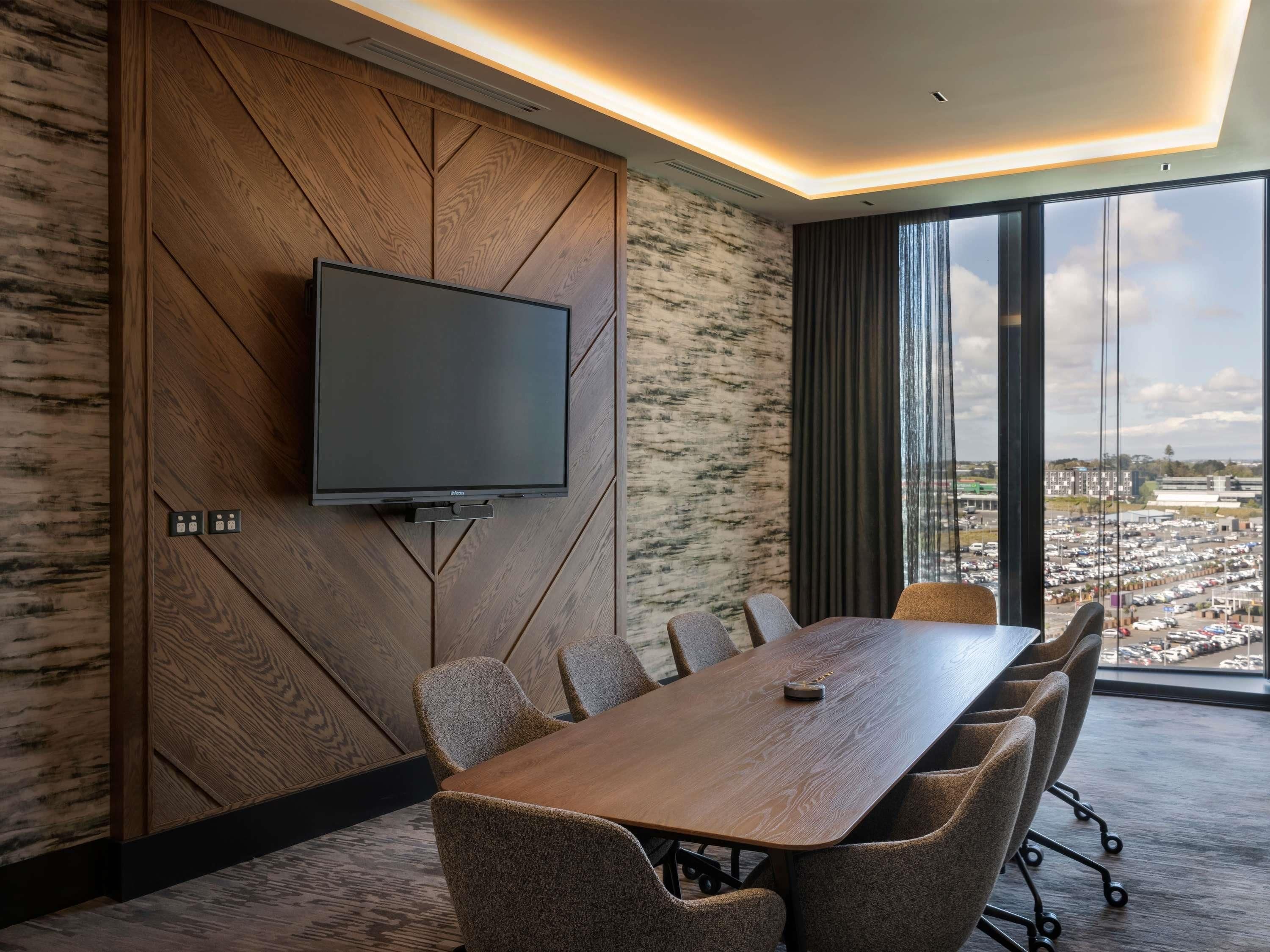 Ein Konferenzraum mit einem großen Tisch, sechs Stühlen, einem Wand-Fernseher und Blick auf die Stadt durch große Fenster.
