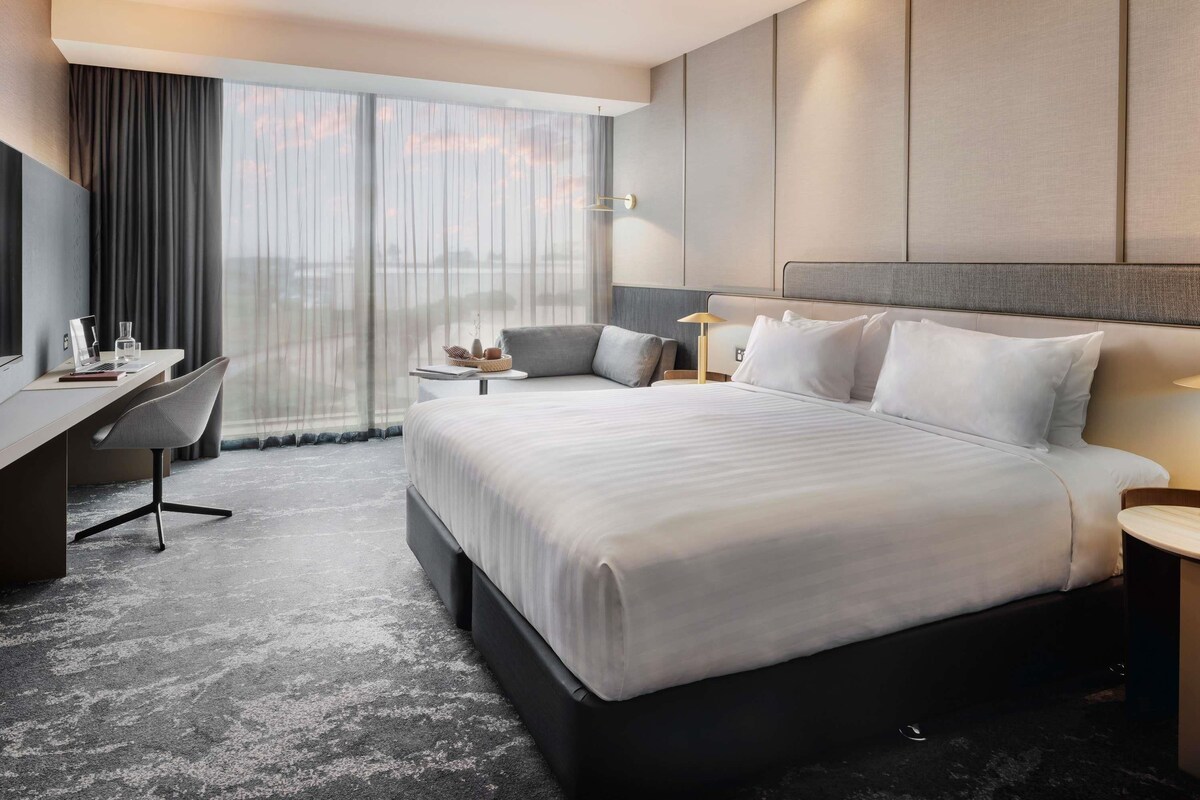 A modern hotel room with a large bed, a desk, and a chair.