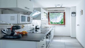 A modern kitchen with white cabinetry, a microwave, a kettle, and a window with a view of greenery. - Holiday apartment close to the center (Njivice)