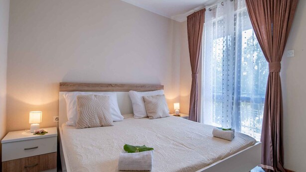 A bedroom with a large bed, two bedside tables, a nightstand, and a window with curtains. - Holiday apartment close to the center (Njivice)