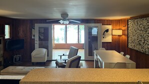 A room with a dining table, chairs, a sofa, a television, and a ceiling fan. - Lakefront Log Cabin with Contemporary touches (Carp Lake)