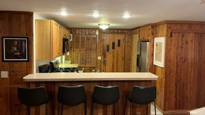A kitchen with wooden paneling, a central island with bar stools, a refrigerator, and a microwave. - Lakefront Log Cabin with Contemporary touches (Carp Lake)
