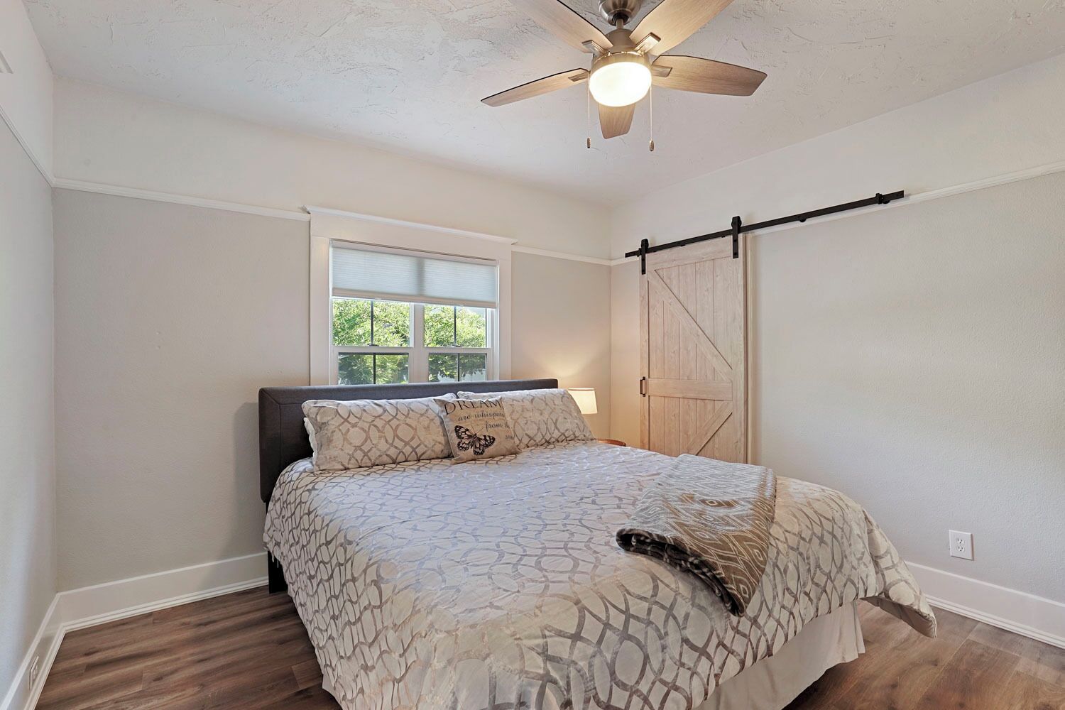 A bedroom with a bed, a ceiling fan, a window, and a wooden door.