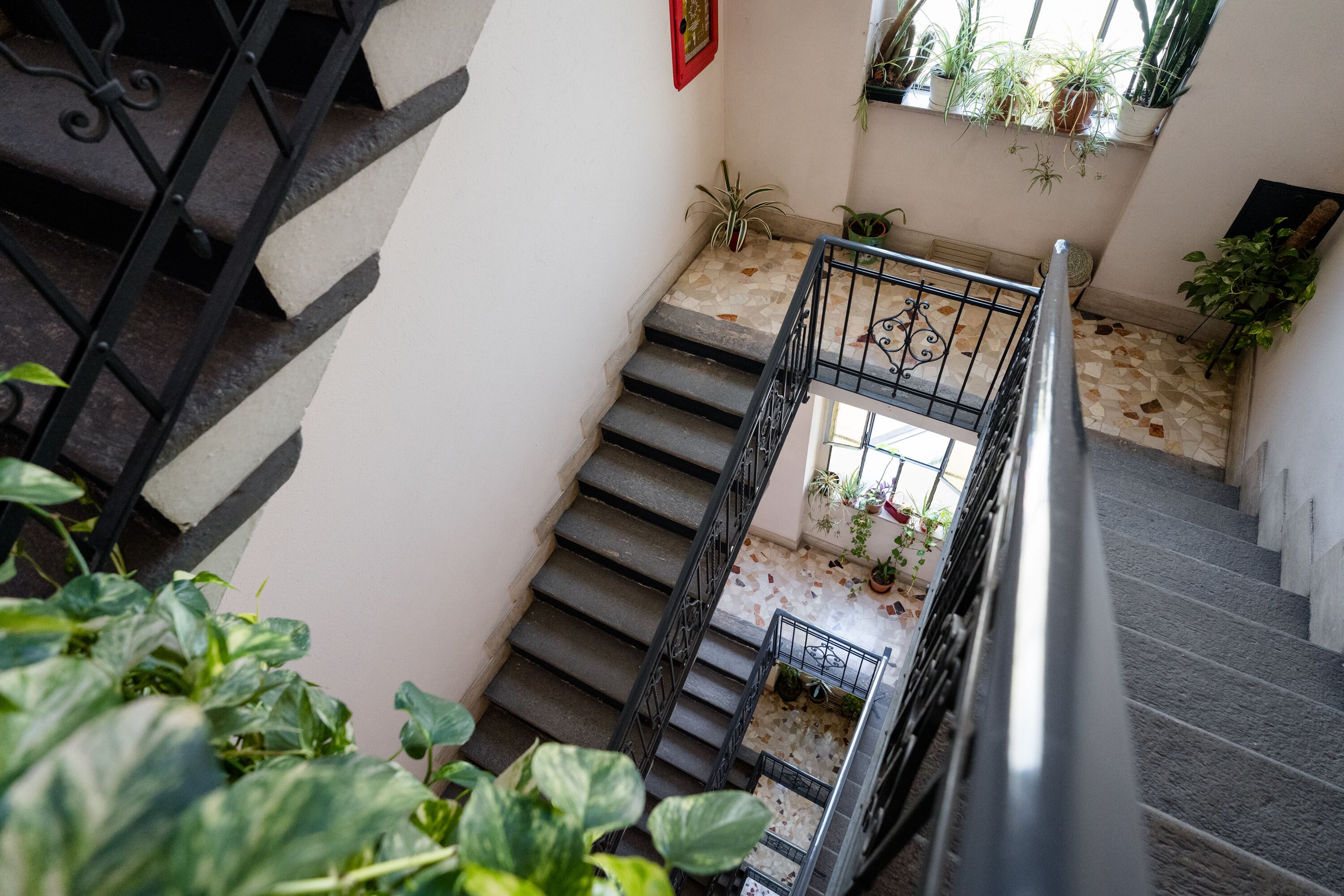 A staircase with a metal railing, potted plants, and a tiled floor.