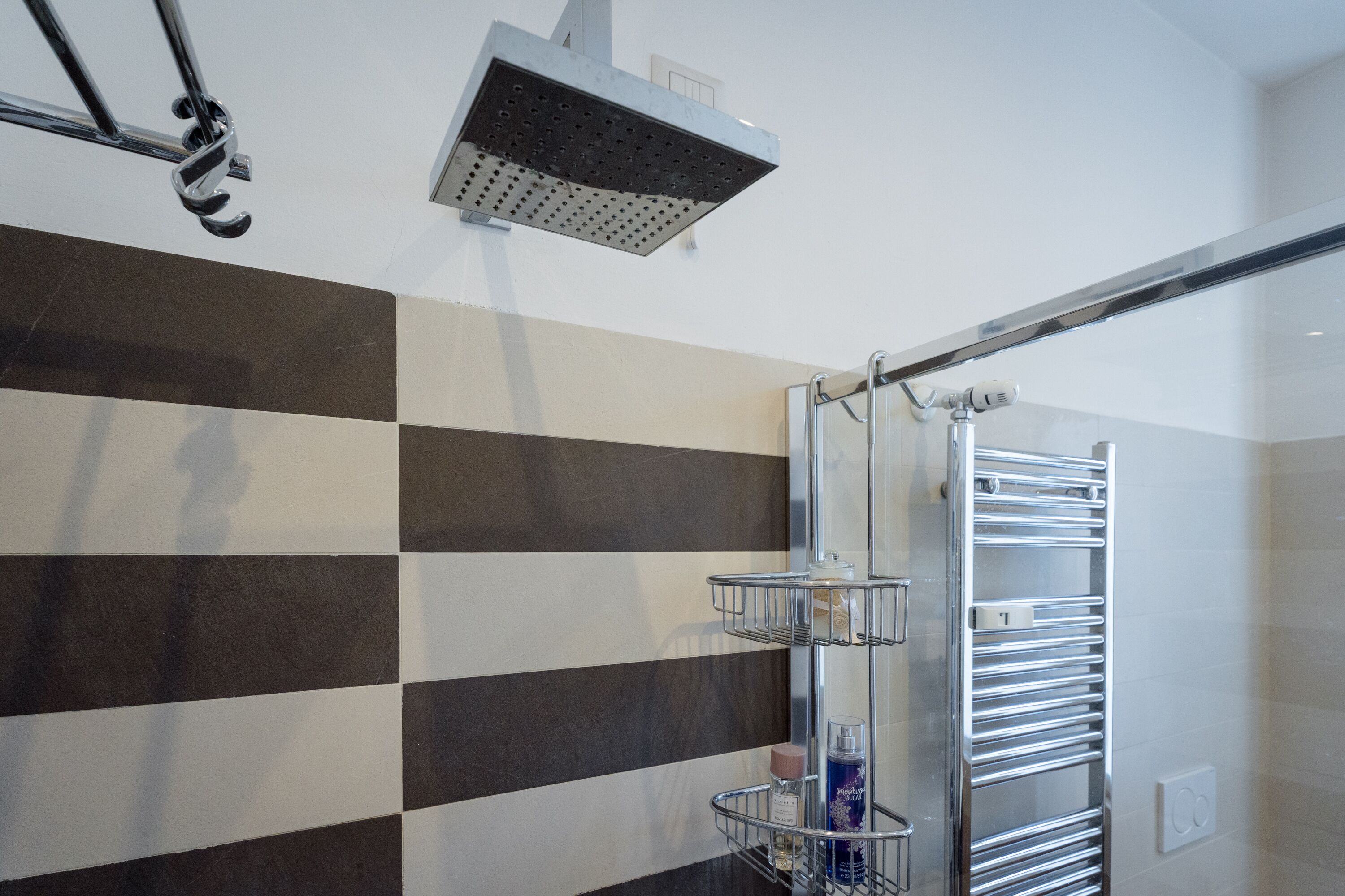 Un baño moderno con pared de azulejos a cuadros, un cabezal de ducha y un perchero con varios estantes.