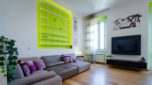 A modern living room with a grey sectional sofa, a bright green shelving unit, a flat-screen TV, and a window with striped curtains. - notaMi - Romolo Space Navigli (Milan)