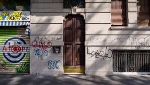 A building facade with a closed metal shutter, a brown door, and various graffiti. - notaMi - Romolo Space Navigli (Milan)