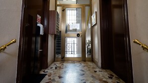 A narrow hallway with a tiled floor, wooden doors with brass handles, and a view into a room with a window and a door. - notaMi - Romolo Space Navigli (Milan)
