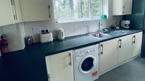 A compact kitchen with a built-in washer, a window with a view of trees, and a toaster on the counter. - Stunning 2-bed Apartment in Crawley (Crawley)