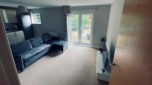 A compact living space with a sofa, a small kitchen area, and a sliding glass door leading to an outdoor area. - Stunning 2-bed Apartment in Crawley (Crawley)