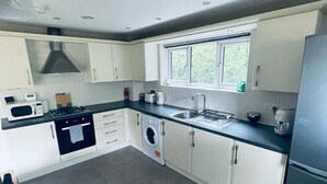 A modern kitchen with white cabinets, a built-in washing machine, a microwave, and a stainless steel refrigerator. - Stunning 2-bed Apartment in Crawley (Crawley)