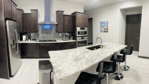 A modern kitchen with dark wood cabinets, stainless steel appliances, a marble countertop, and a bar area with stools.