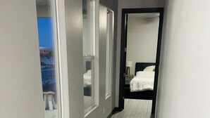 A hallway with large windows, a bed in the background, and a view of a building outside.