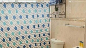 Une salle de bain avec un rideau de douche à motifs, des toilettes, un lavabo avec un meuble de rangement et un petit tapis sur le sol.