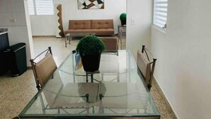 Un coin repas avec une table et des chaises en verre, un canapé marron et une plante verte au centre.