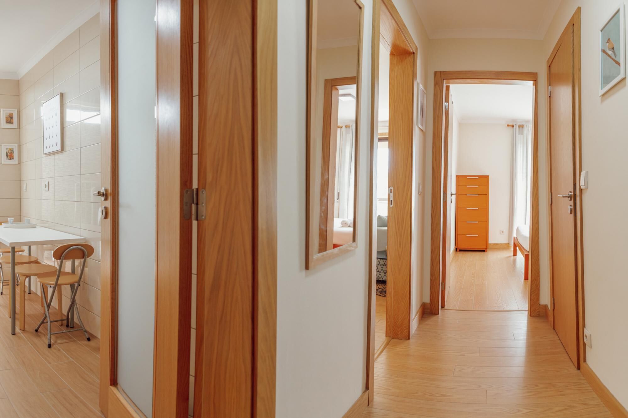 A hallway with wooden doors leading to bedrooms, a small dining area with chairs, and a wooden dresser.