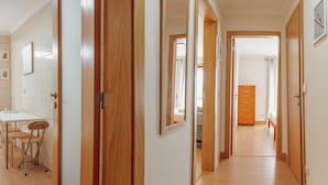 A hallway with wooden doors leading to bedrooms, a small dining area with chairs, and a wooden dresser. - Bright Apartment by Homing (Porto)