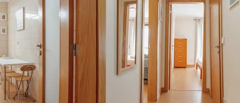 A hallway with wooden doors leading to bedrooms, a small dining area with chairs, and a wooden dresser.