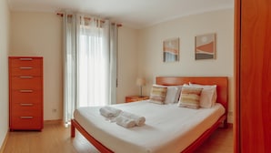 A hotel room with a large bed, a wooden dresser, and two wall-mounted paintings. - Bright Apartment by Homing (Porto)
