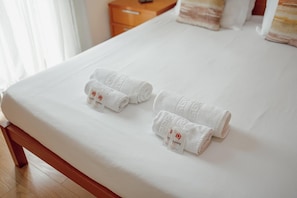 Ein ordentlich bezogenes Bett mit zwei aufgerollten Handtüchern und zwei kleinen Kosmetiksets auf einer weißen Bettdecke.