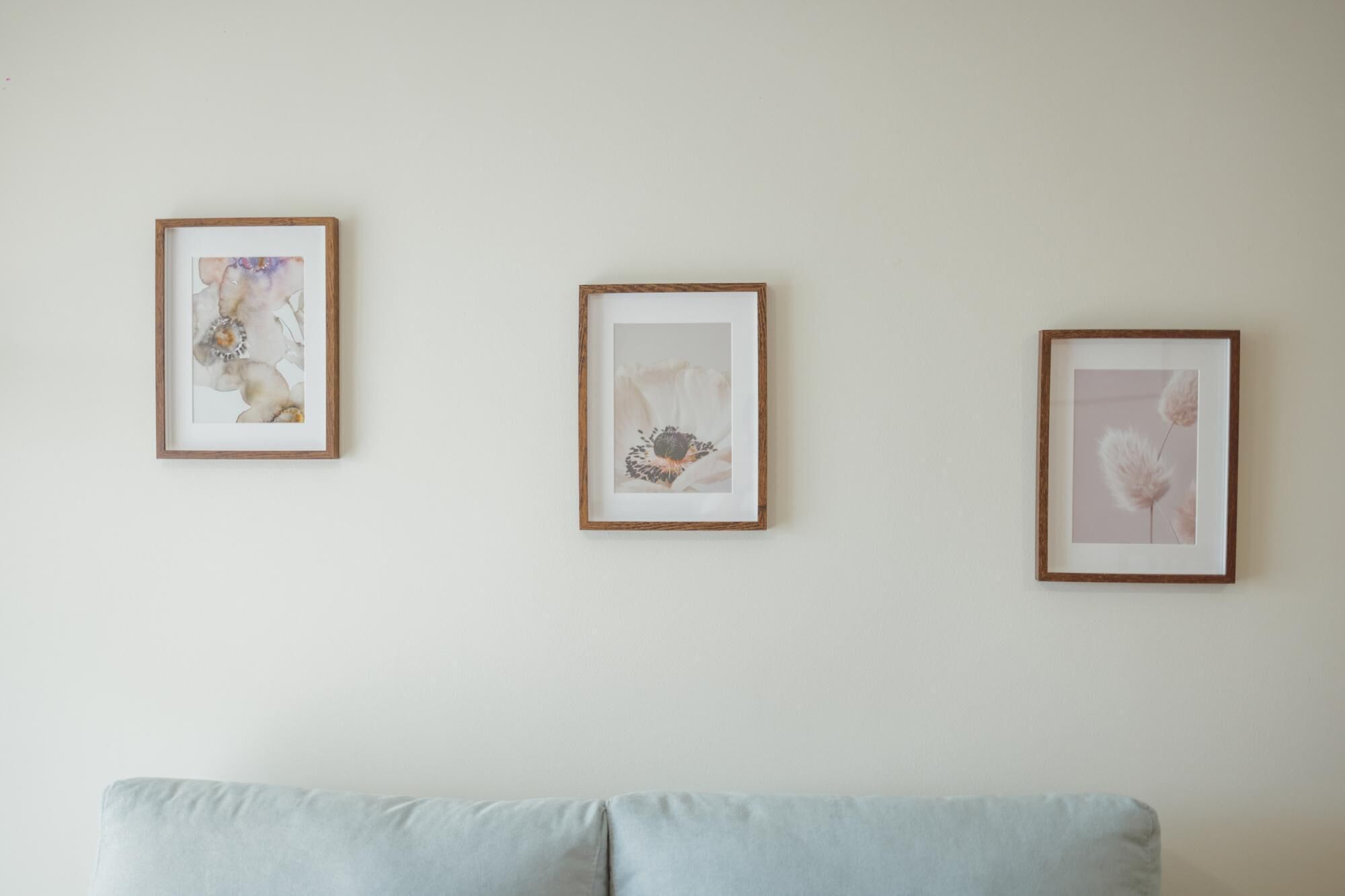 Three framed artworks on a wall above a light blue sofa.