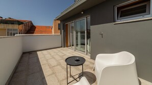 Ein Balkon mit weißem Stuhl, einem kleinen runden Tisch und einer Schiebeglastür.