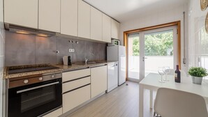 Eine moderne Küche mit Einbauofen, Kaffeemaschine und Kühlschrank. Ein Essbereich mit Tisch und Stühlen lädt zum Verweilen ein, und ein Fenster bietet Blick auf Grünflächen.