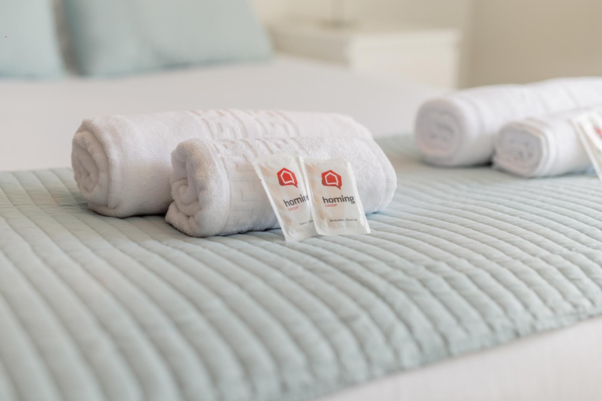 A neatly made bed with rolled white towels and two packets of 'homing' shower gel.