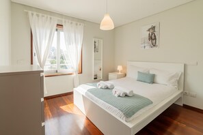 Un dormitorio ordenado con cama, mesita de noche y ventana con cortinas.