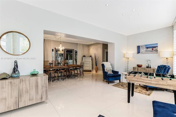 A spacious living area with a dining table, sofas, and a foosball table. - Luxurious 4Bdr with a pool, blocks to beach (Surfside)