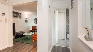 Un interior moderno con una sala de estar que incluye un sofá, un sillón y una mesa de centro. Un pasillo conduce a un baño con ducha y espejo.